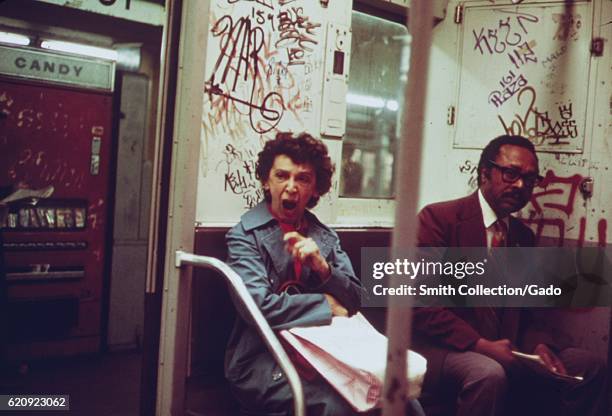 Mature African-American man and a mature Caucasian woman sit inside a subway car which has been extensively marked with graffiti, New York City, New...