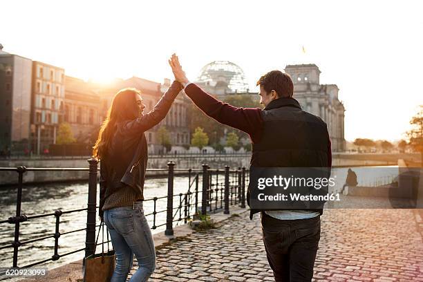 germany, berlin, young walking along river spree high fiving - berlin spree stockfoto's en -beelden