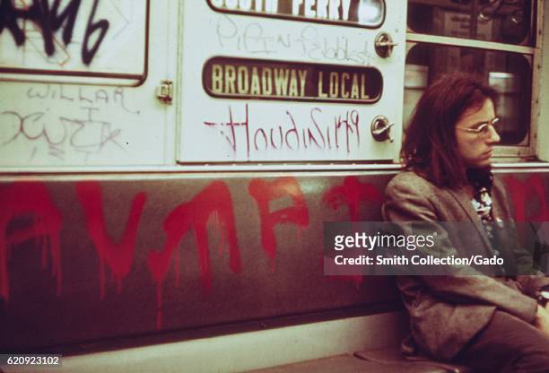 Man with long hair sits on a seat on a subway car which has been extensively marked with graffiti, New York City, New York, May, 1973. Image courtesy...