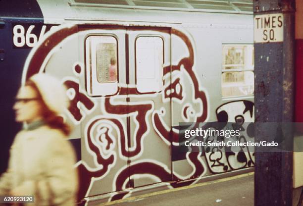 Woman walks past a subway train covered in graffiti, in the Times Square subway station, New York City, New York, May, 1973. Image courtesy National...
