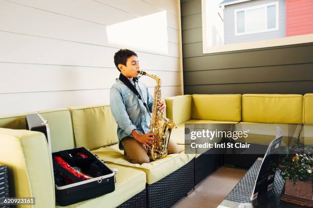 mixed race boy playing saxophone on sofa - saxophone stock pictures, royalty-free photos & images