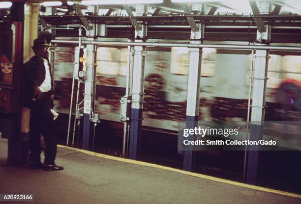 An African-American man stands on a subway station platform as a subway train car, covered in graffiti, passes by in New York City, New York, May,...