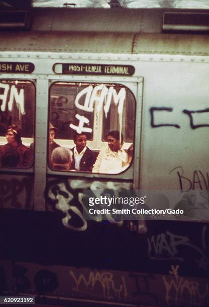 Passengers are visible through the window of a subway car which has been covered in graffiti, New York City, New York, May, 1974. Image courtesy...
