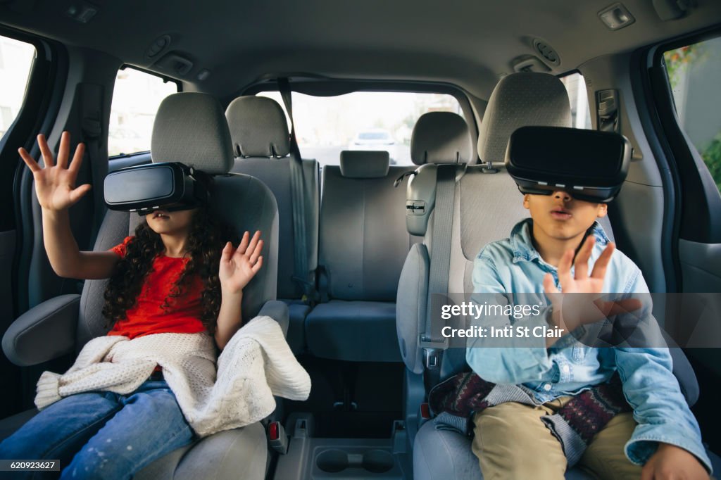 Mixed race children using virtual reality goggles in car