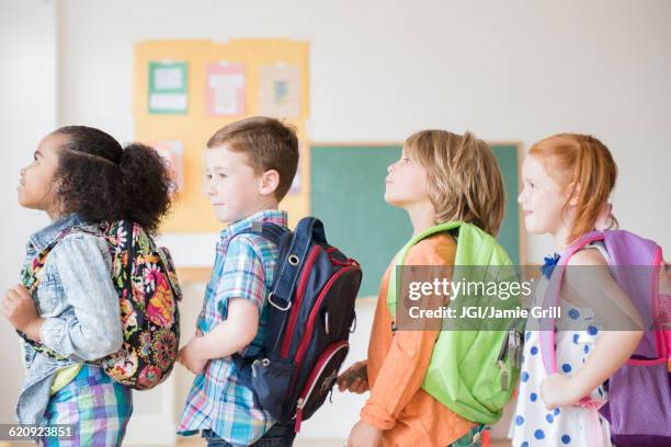 students wearing backpacks in classroom - comienzo del año escolar fotografías e imágenes de stock
