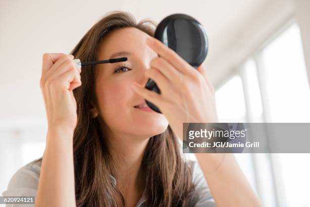 mixed race woman applying makeup in compact mirror - mascaras 個照片及圖片檔