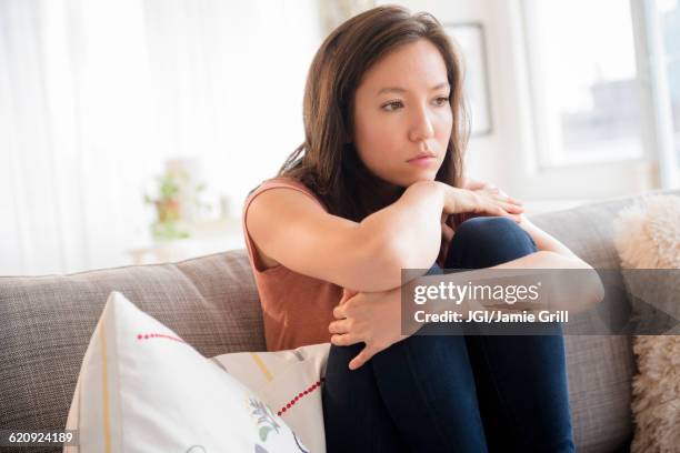 sad mixed race woman sitting on sofa - asian woman angry foto e immagini stock