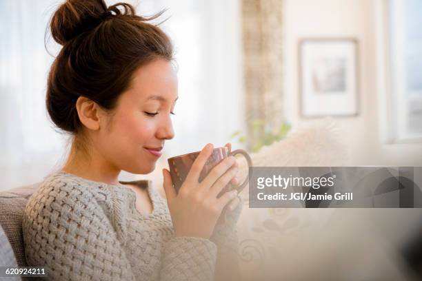 mixed race woman drinking coffee on sofa - woman drinking coffee at home stock-fotos und bilder