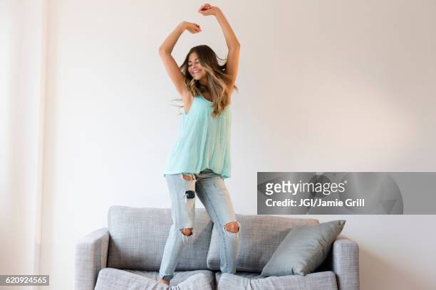 mixed race woman jumping on sofa - celebrate living stockfoto's en -beelden