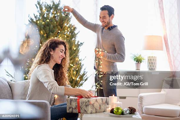 couple decorating for christmas in living room - decorating the christmas tree stock pictures, royalty-free photos & images