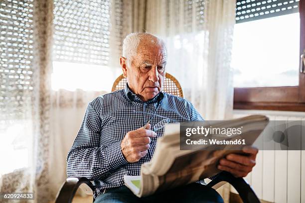 senior man reading newspaper at home - cadeira de balanço - fotografias e filmes do acervo