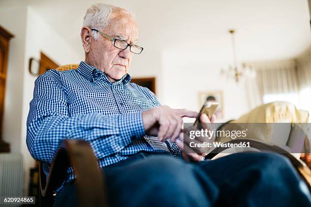 senior man using smartphone at home - schaukelstuhl stock-fotos und bilder