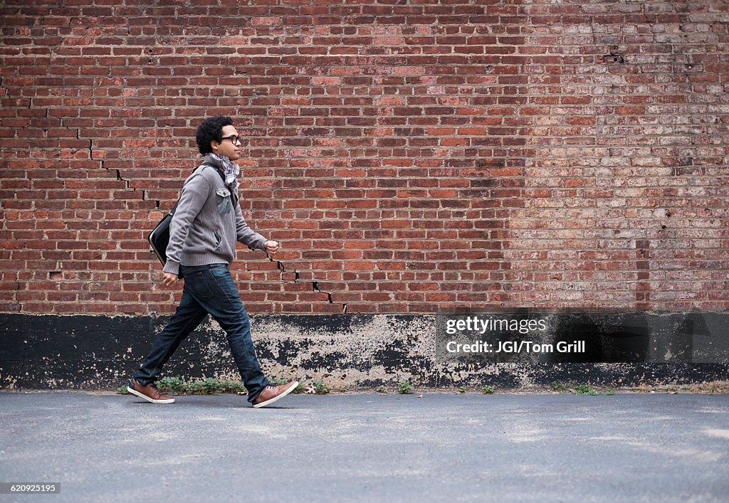 Mixed race man walking near brick wall