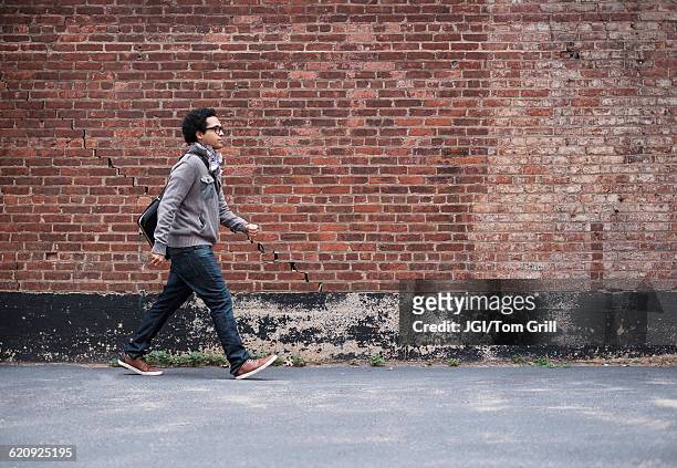 mixed race man walking near brick wall - walking side by side stockfoto's en -beelden