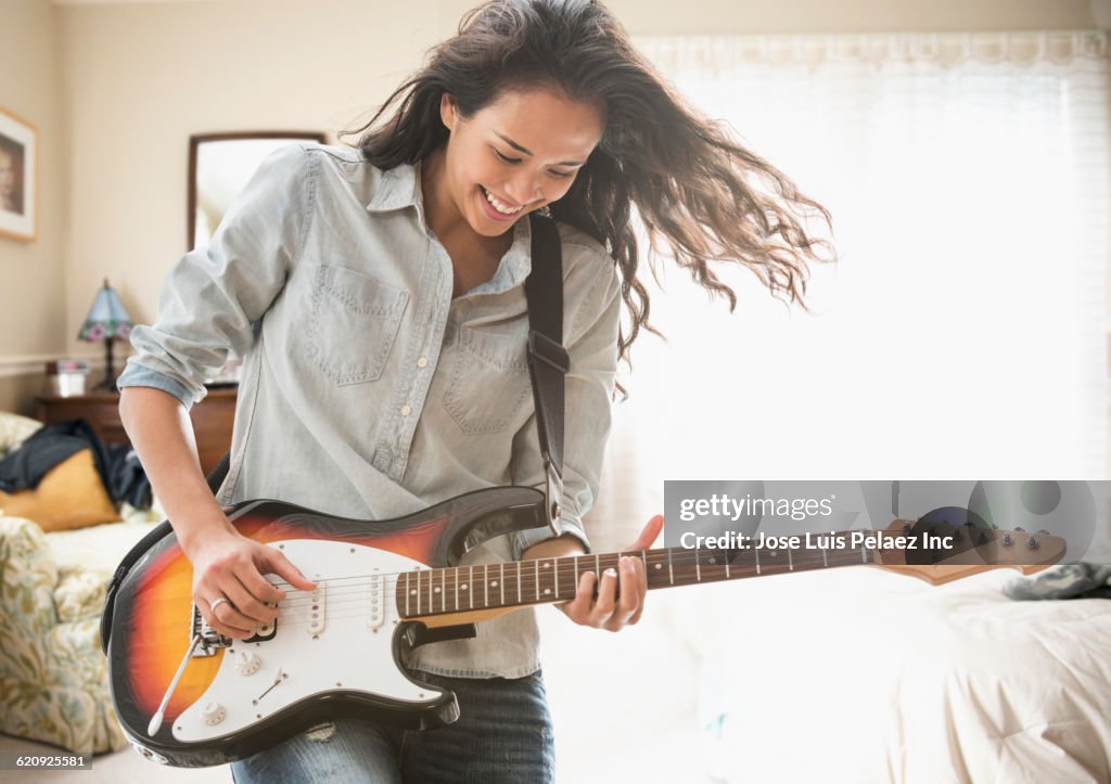 Mixed race woman playing electric guitar