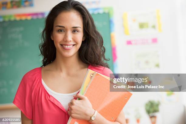 mixed race teacher holding books in classroom - enseignante photos et images de collection