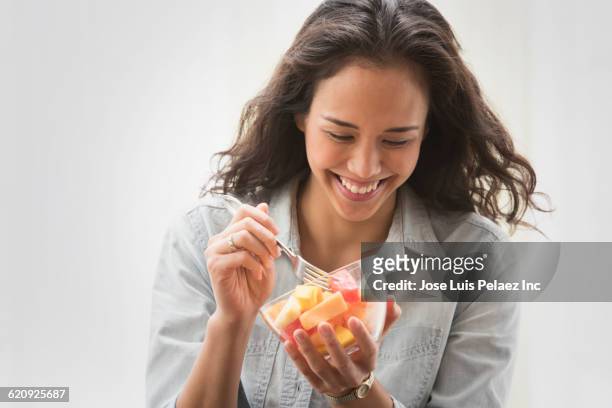 mixed race woman eating fruit salad - woman eating fruit imagens e fotografias de stock