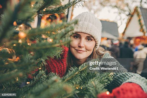 woman looking trough conifer branches on the christmas market - keulen stockfoto's en -beelden