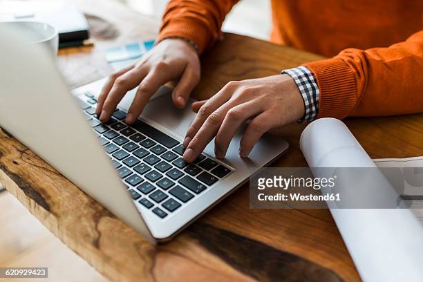 close-up of man using laptop next to construction plan at desk - hand close up stock-fotos und bilder