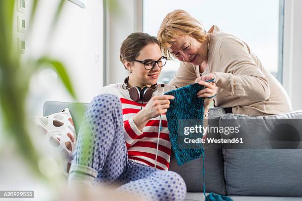 young woman sitting on couch showing knitwear to senior woman - old granny knitting stock-fotos und bilder