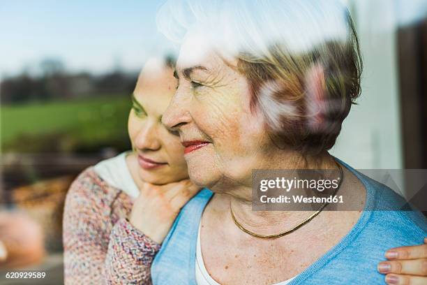 young woman and senior woman behind windowpane - granddaughter stockfoto's en -beelden