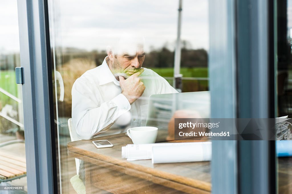 Businessman with laptop at wooden table thinking