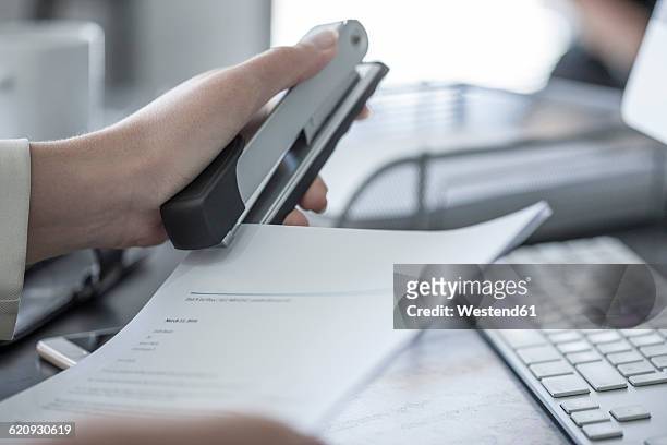 close-up of woman at desk stapling a document - staples office stockfoto's en -beelden
