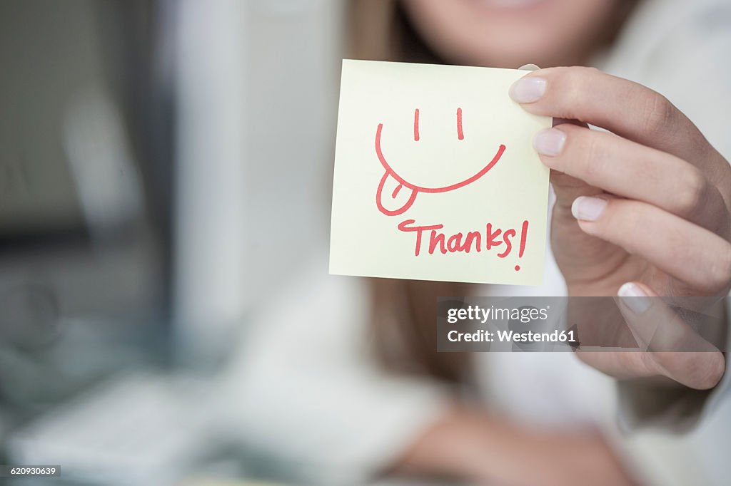 Close-up of woman holding a sticky note with a smiley face