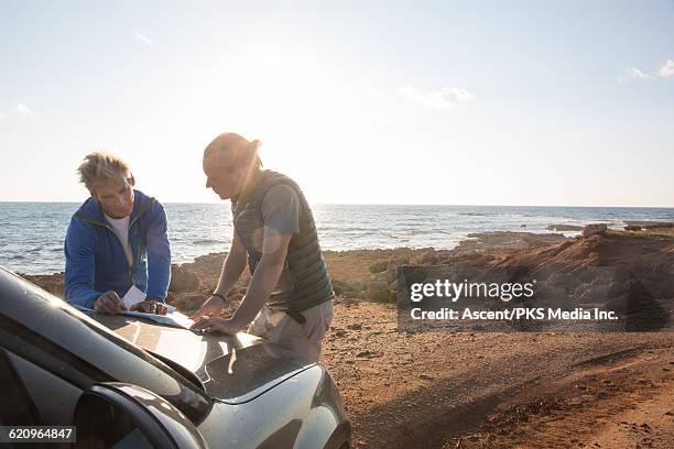 father and son plot route on hood of suv, seaside - dirty car stockfoto's en -beelden