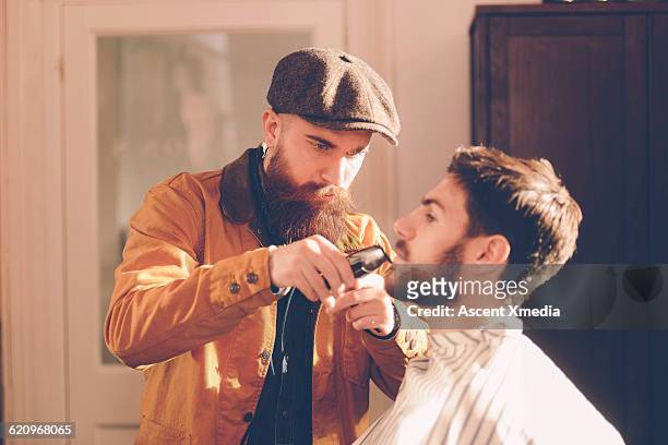hip stylist trims customer's beard in barber shop - rasieren stock-fotos und bilder