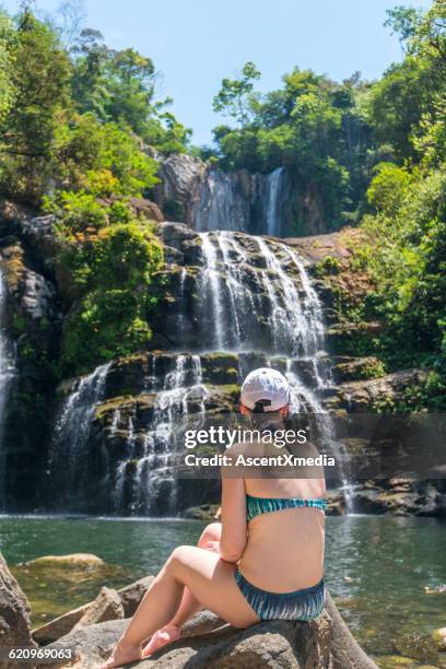 woman relaxes by pool, looks up to waterfall - costa rica waterfall stock pictures, royalty-free photos & images