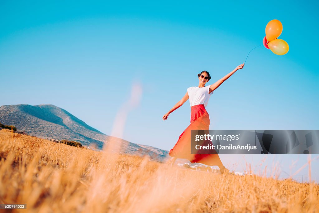Cheerful young woman walking in the field holding balloons