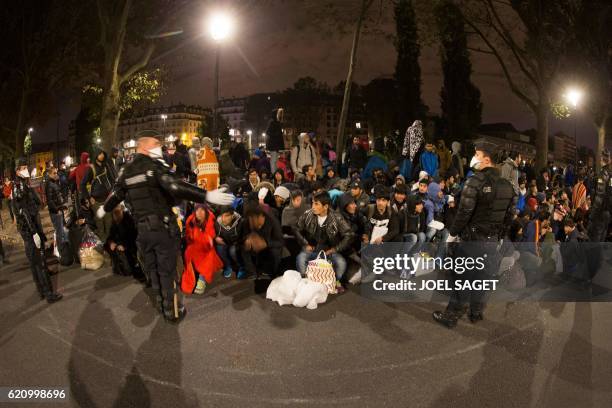 Migrants, mostly from Afghanistan, sit near police during the evacuation of a makeshift camp in Paris on November 4 near to the Stalingrad metro...