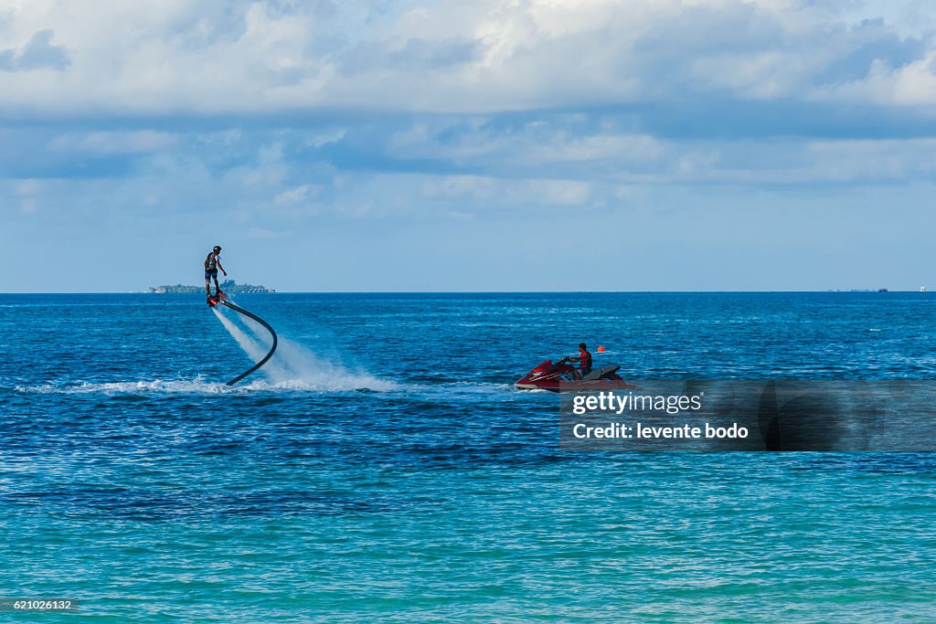 Fly board and jet ski in the blue lagoon. Silhouette of a fly board rider at sea. Professional rider is playing with a new water sport called fly board. Tropical summer water-sport activity.