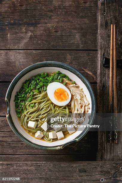 ceramic bowl of asian style soup with green tea soba noodles, egg, mushrooms, spring onion and tofu cheese, served with chopsticks over old wooden background. top view, copy space - miso stock-fotos und bilder