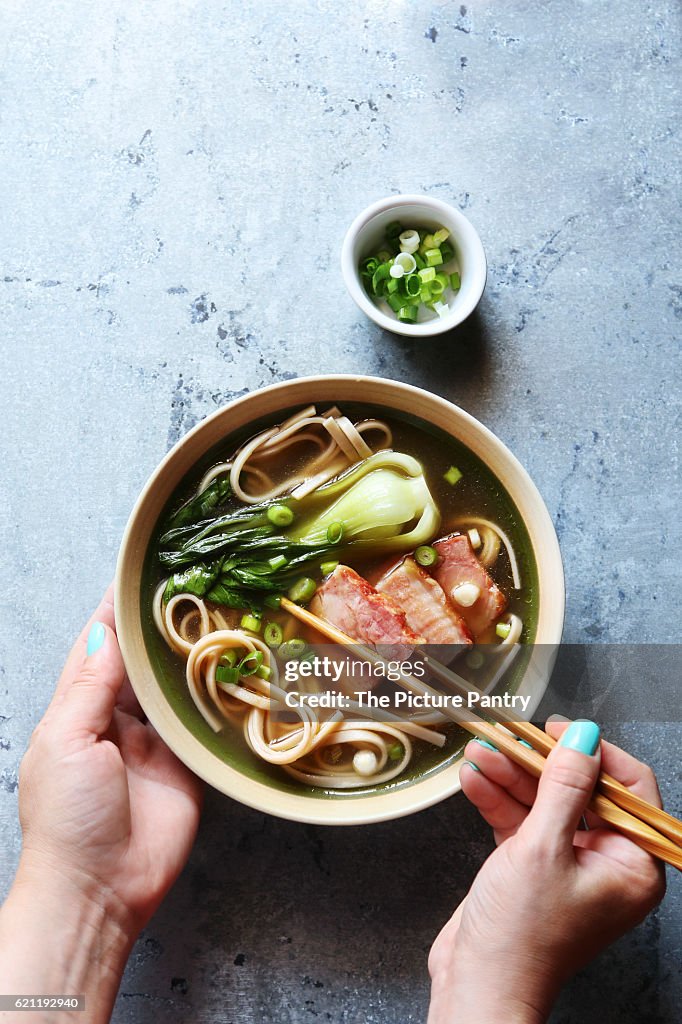 Female hands holding a bowl of pork belly udon noodle soup.Top view