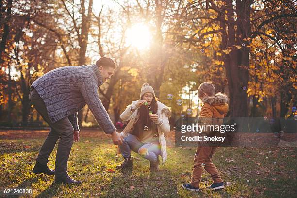 happy family blowing bubbles - fall park stock pictures, royalty-free photos & images