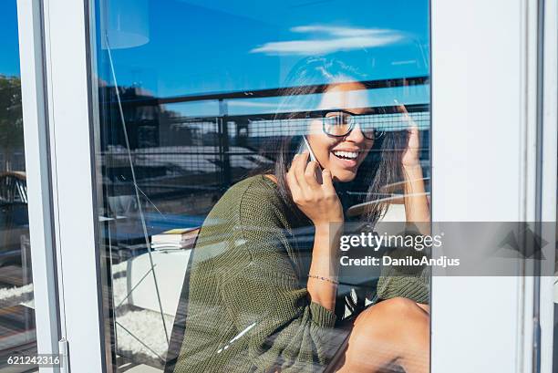 beautiful young woman talking on her smartphone - sun rays through window bildbanksfoton och bilder