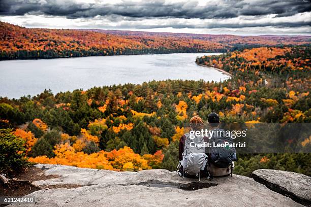 pareja joven haciendo senderismo en la montaña y relajante mirando a la vista - adventure fotografías e imágenes de stock