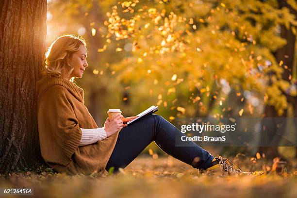 entspannte frau liest ein buch im herbsttag. - frau mittleren alters stock-fotos und bilder