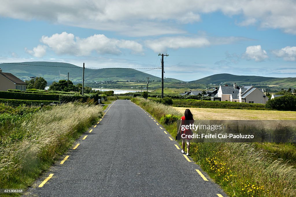 A woman in a red dress walking on roadside of Waterville in Ireland