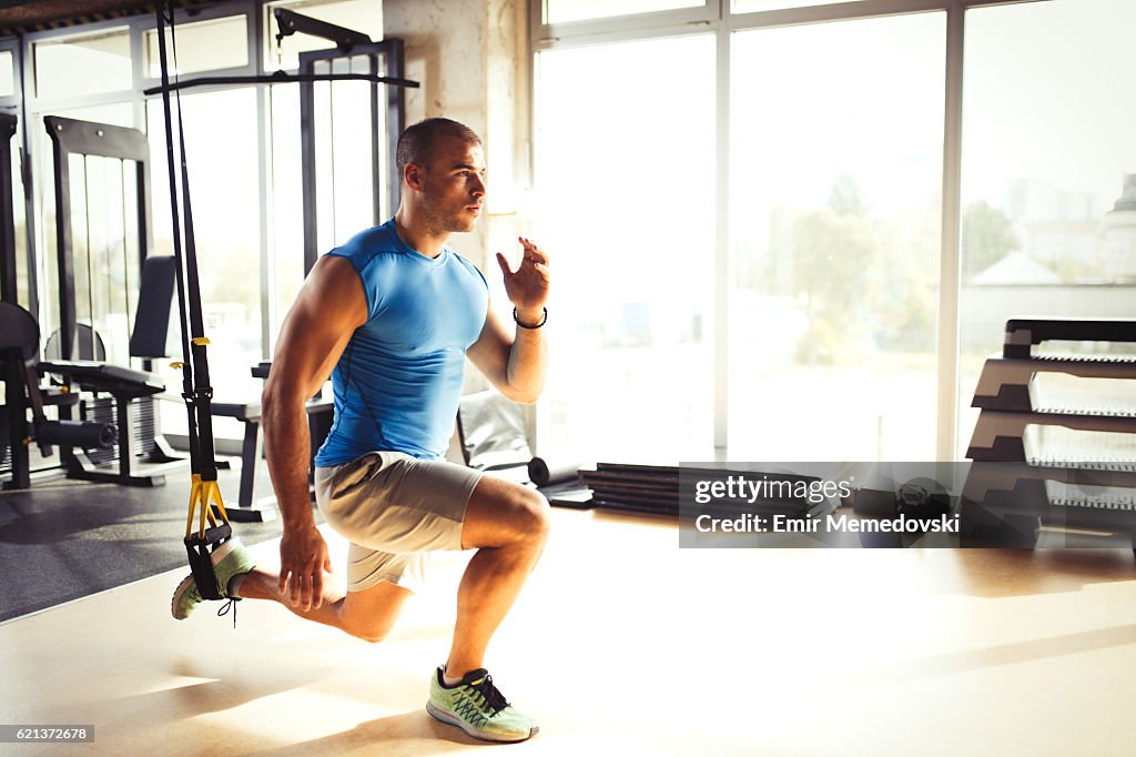 Man doing leg exercises with suspension straps at gym.