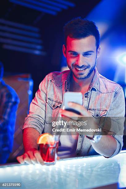 cheerful man having cocktail while text messaging in nightclub - man party night bar posing stock pictures, royalty-free photos & images