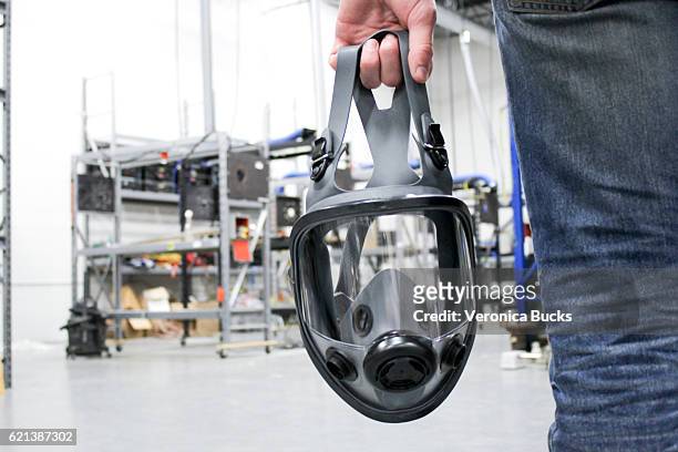 a man holding a respirator mask in an industrial facility - atemschutz stock-fotos und bilder
