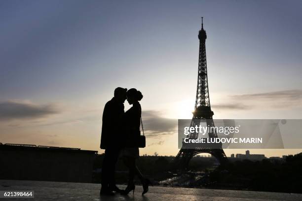 Man and a woman kiss in front of the Eiffel Tower, on the Parvis des Droits de l'Homme square in Paris on November 6, 2016. / AFP / LUDOVIC MARIN