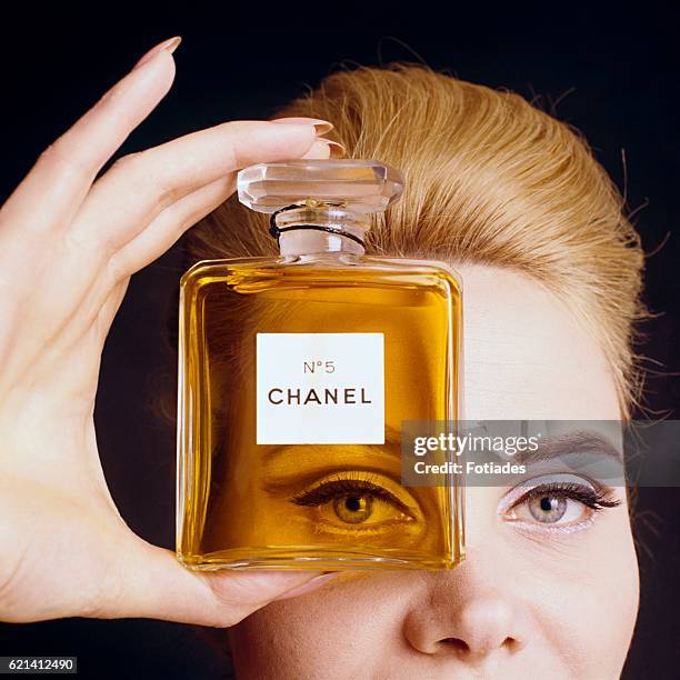 Close up of model holding a bottle of Chanel No. 5 perfume up to her eye as if looking through the bottle.