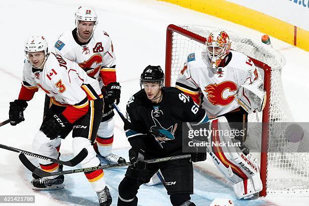 Melker Karlsson of the San Jose Sharks and Jyrki Jokipakka and Jyrki Jokipakka of the Calgary Flames look while Chad Johnson of the Calgary Flames...