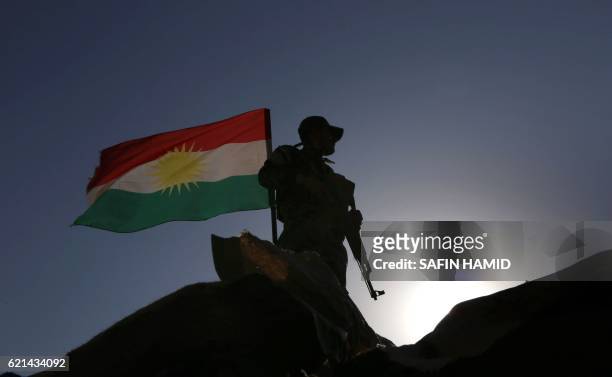 An Iraqi Kurdish Peshmerga fighter, next to a Kurdish flag, holds a position in Sheikh Ali village near the town of Bashiqa, some 25 kilometres north...