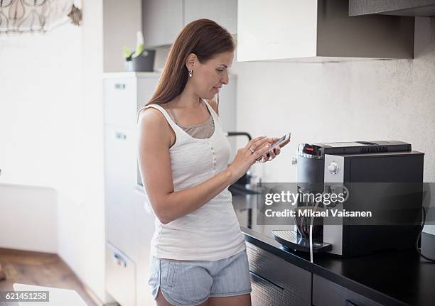 portait of woman in kitchen with smartphone and espresso machine - caffettiera foto e immagini stock