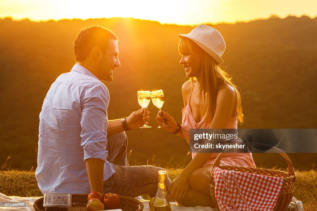 Smiling couple toasting with wine on picnic at sunset.